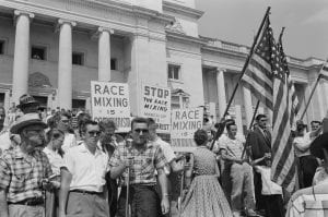 Little Rock, 1959. Rally at state capitol, protesting the integration of Central High School. Protesters carry US flags and signs reading "Race Mixing is Communism" and "Stop the Race Mixing March of the Anti-Christ".