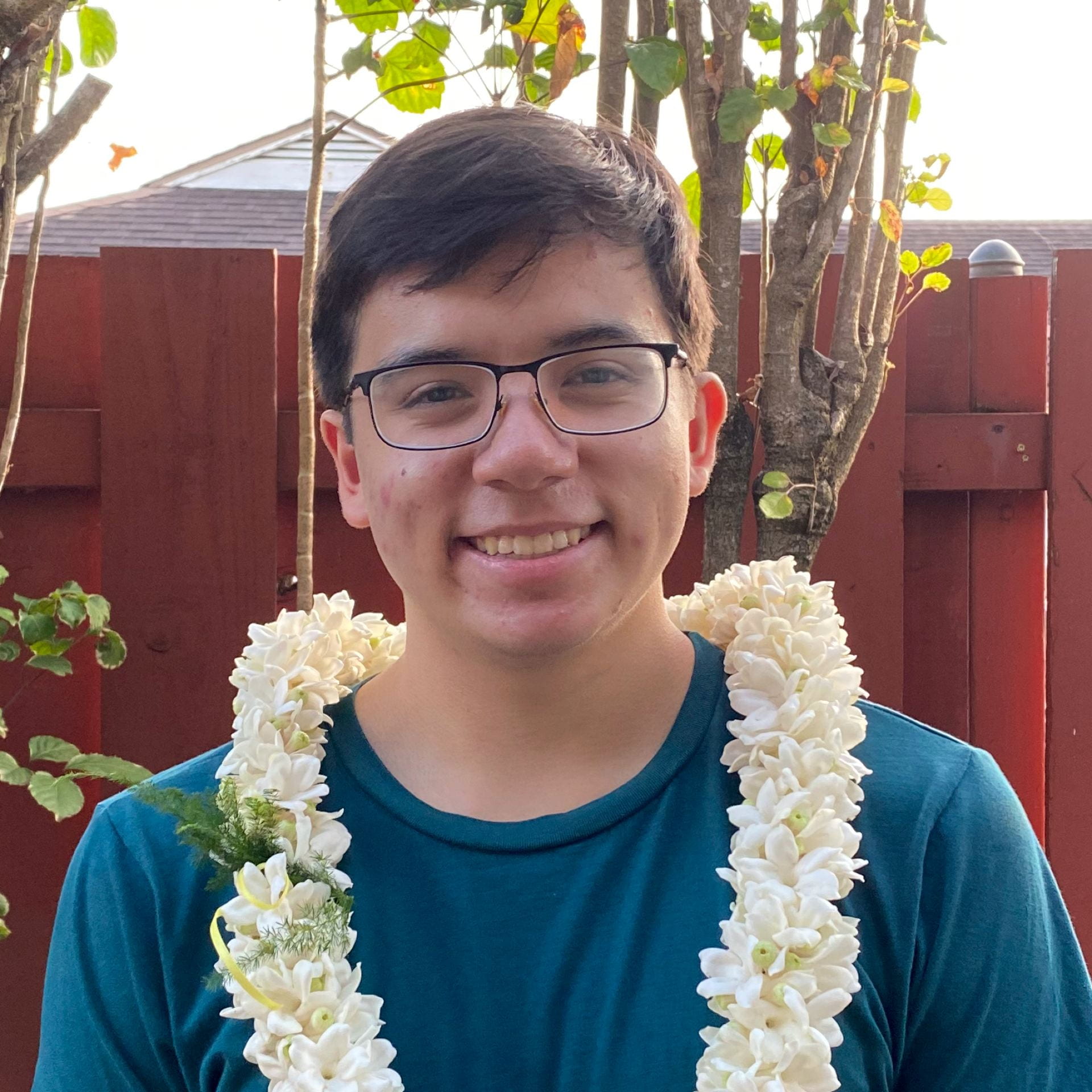 Photo of young man with glasses wearing a traditional Hawaiian lei.