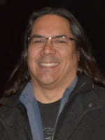 Photo of man smiling with long dark hair wearing glasses.