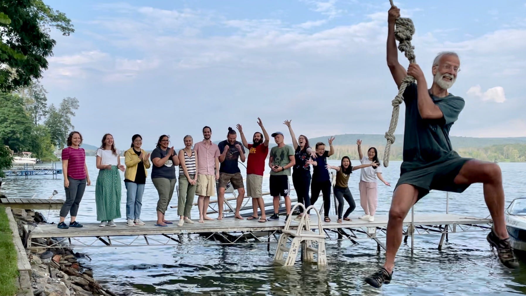 Lab members cheer from the dock while Andy Clark swings over the lake from a rope.