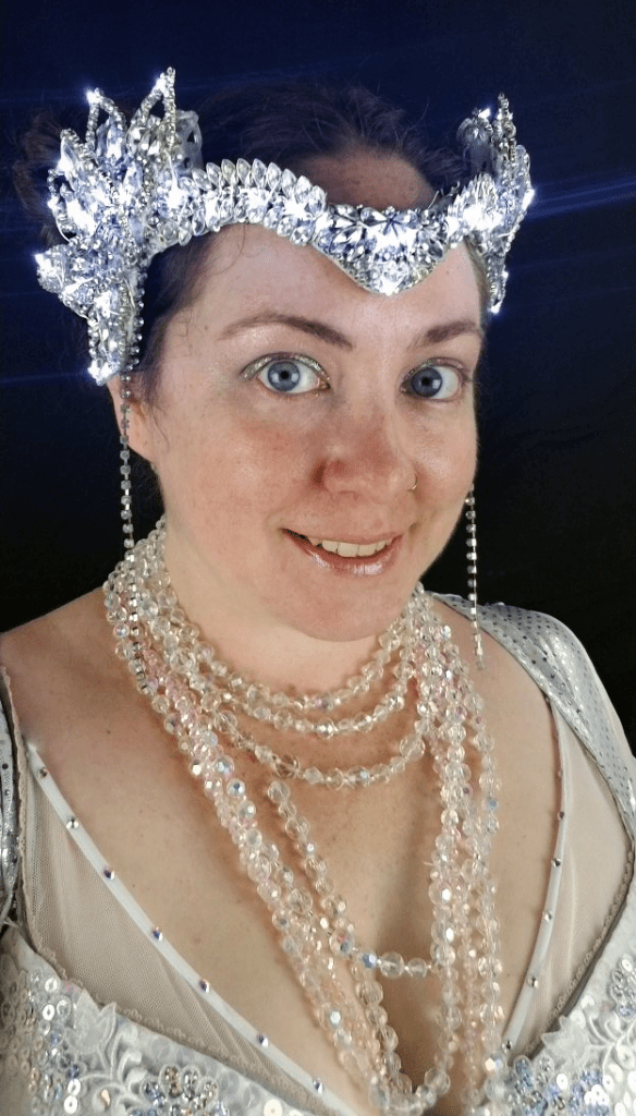 A headshot of a woman in a white and silver costume and headpiece