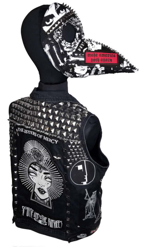 A studded vest and beaked mask, both covered in band patches and studs