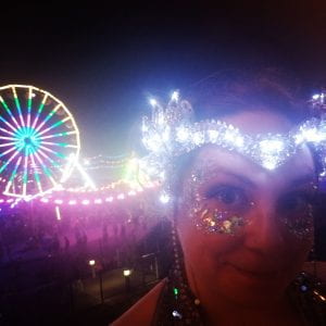 A woman's face with a sparkly light up head piece and ferris wheel in the background