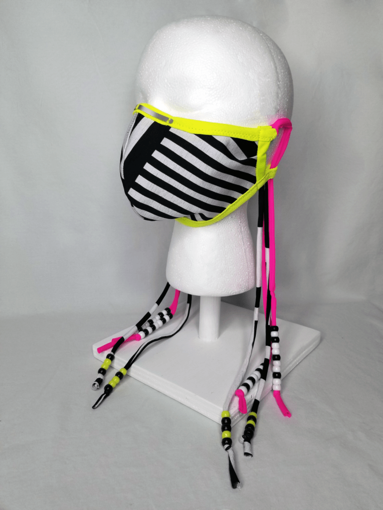 A striped face mask on a head form in black, white, neon yellow, and neon pink with beaded ties.
