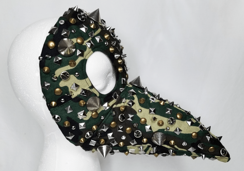 A camo plague doctor mask covered in studs and spikes