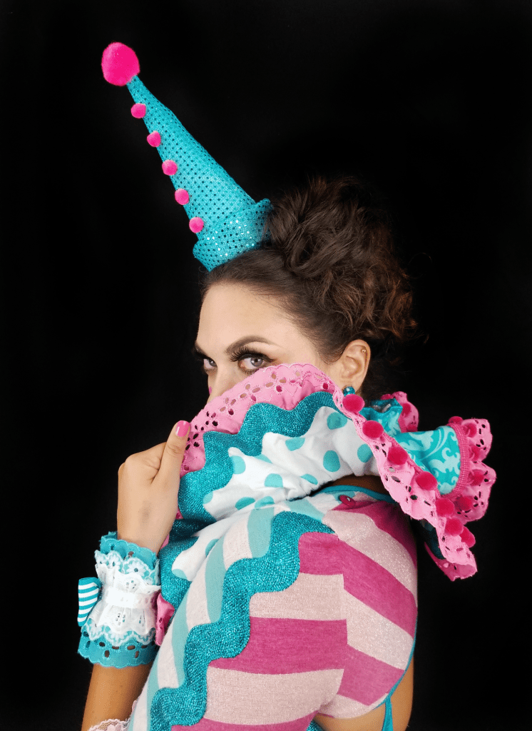 A woman in a clown costume peering over a ruffle collar.