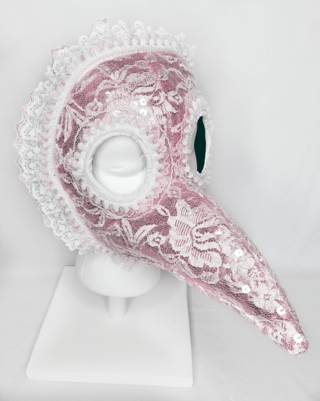 A pink and white lace beaked mask with ruffle trim