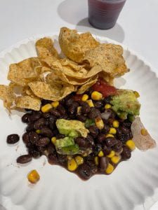 Multigrain tortilla chips and a salad made out of black beans, corn, avocado, and tomatoes on a paper plate.