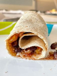 A close-up shot of a rolled up tortilla with a salsa-bean-cheese mixture inside.