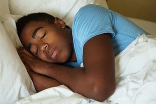 Teen boy sleeping peacefully in bed.
