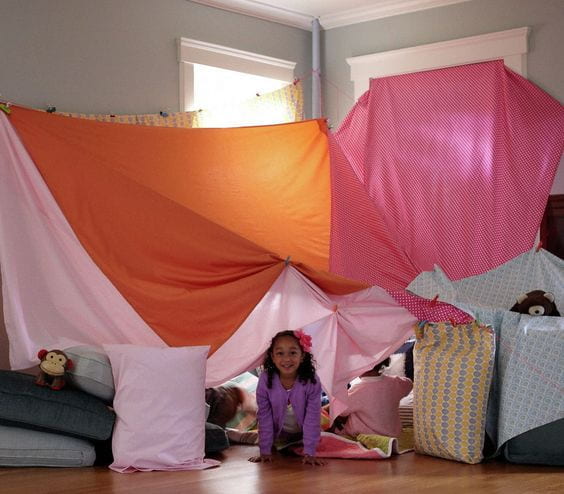 Young girl inside her playfort made from bed sheets draped over furniture