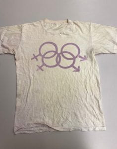A silk screened t-shirt with two male and two female signs interlinked; the symbols are lavender in color.