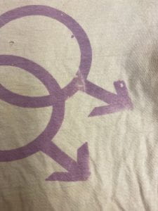 A close-up of the silk screened t-shirt with lavender two male and two female signs interlinked.