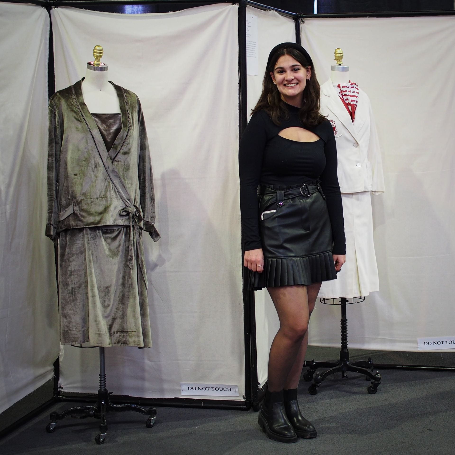 Woman in black skirt and top in front of an exhibit featuring a silver dress from the 1920s to the left. 