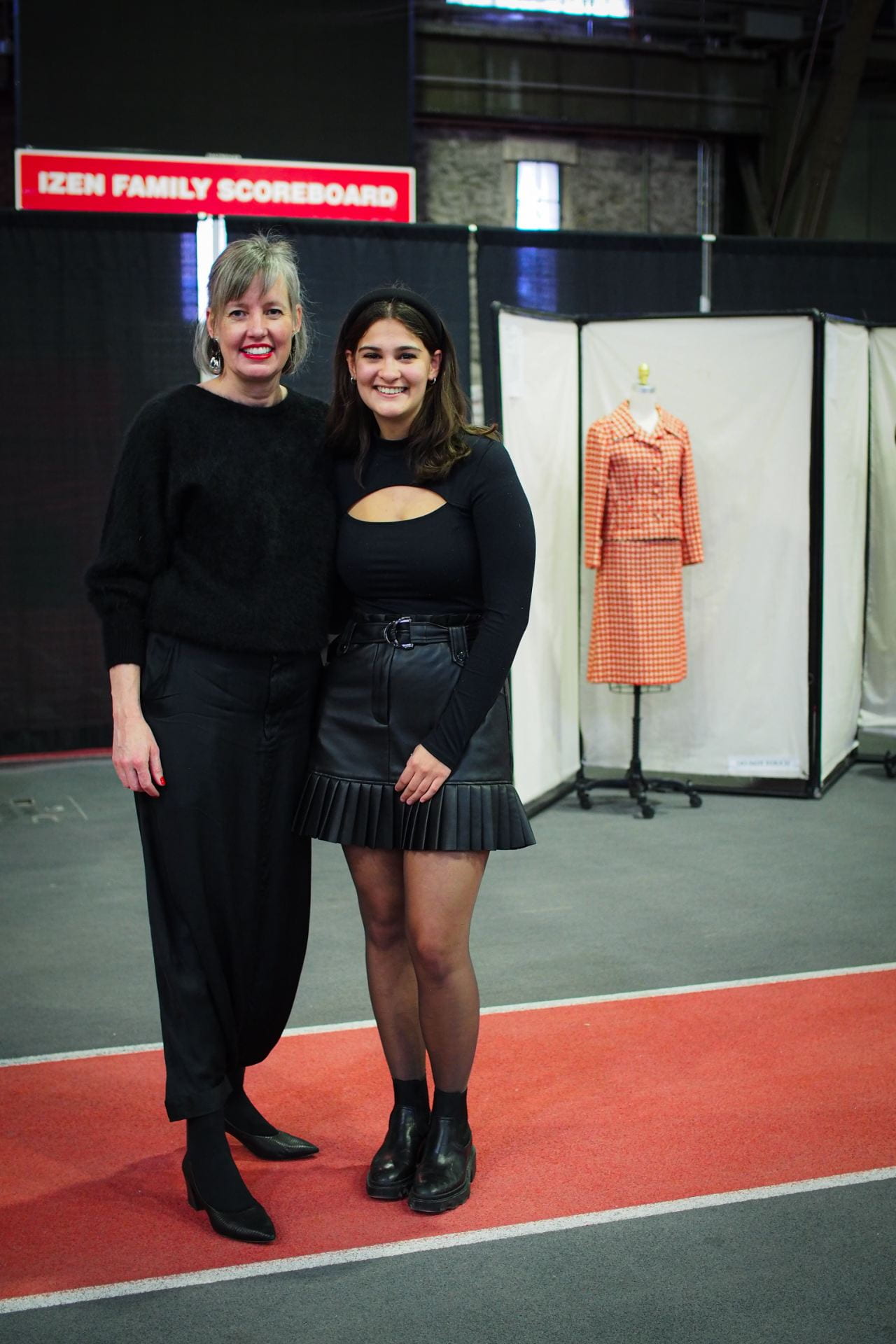 Two people standing in front of garments on dressforms