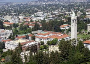 Aerial photography of a college campus made of light stone with reddish terracotta roofs and a talk light stone clock tower on the right side of the photo. 