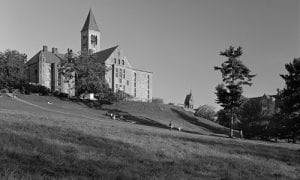 Black and white photo of Cornell University's clocktower from the bottom of a grassy slope.