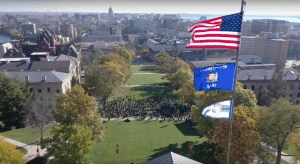 Photo showing the central quad of the University of Wisconsin-Madison from above and in the foreground there are three flags flying on a pole including the United States flag, the state of Wisconsin flag, and the Ho-Chunk Nation flag.