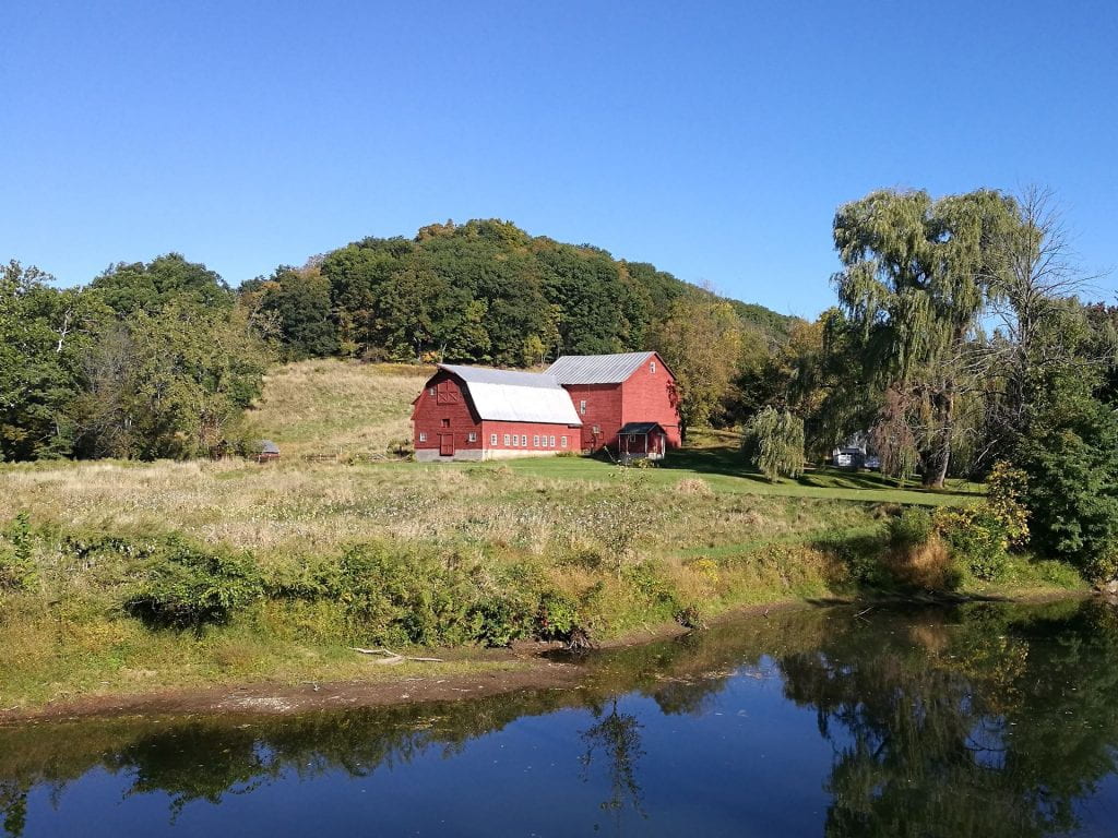 red barn near a body of water, immediately backed by a hill