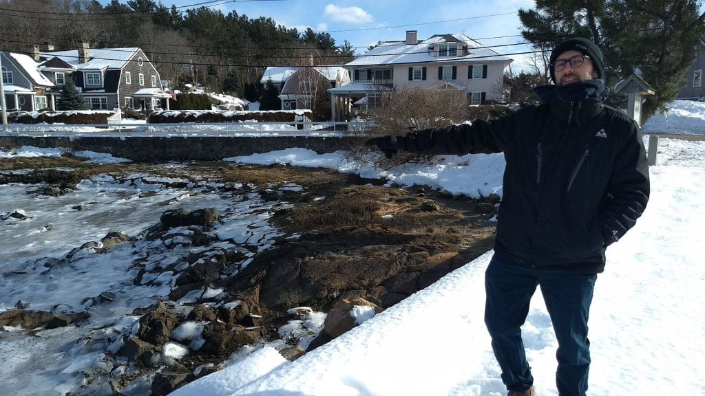 man in winter coat points to frozen waterfront in residential neighborhood