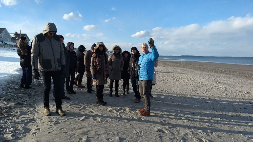 group of people in winter coats touring a beach