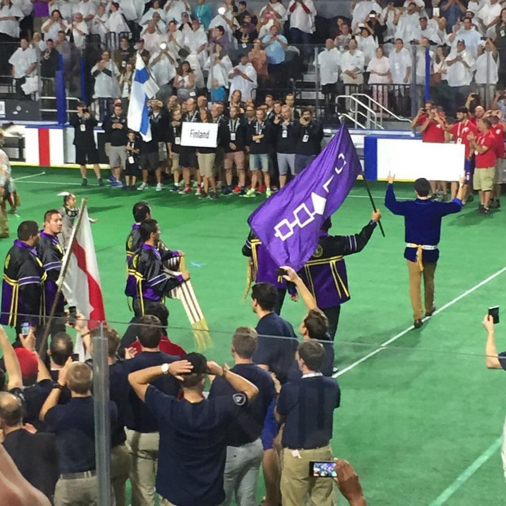 The Iroquois Nationals team waves their flag, which is a cloth representation of what was originally a wampum belt representing the original five nations constituting the Haudenosaunee Confederation. Behind the flagbearers march two players holding the Two-Row Wampum Belt, which is a treaty between the Haudenosaunee and all settlers, promising a policy of peaceful coexistence. Photo courtesy of Fredrick Blaisdell. Source: @FredBlaisdell on Instagram