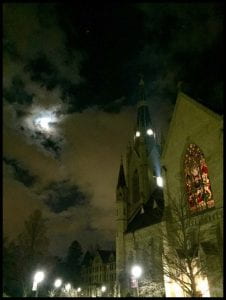 Gothic cathedral at night under a full moon with a cloudy sky