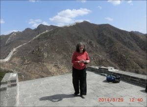 woman stands atop a stonestructure with Great Wall receding in the distance