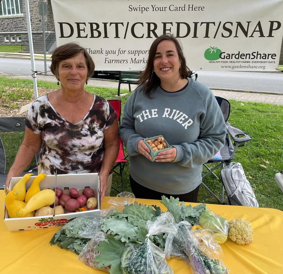 Two people standing at GardenShare farmer's market table with produce.