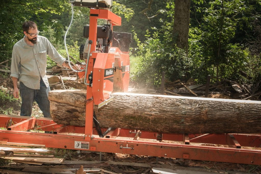 A man runs a log through a saw mill. 