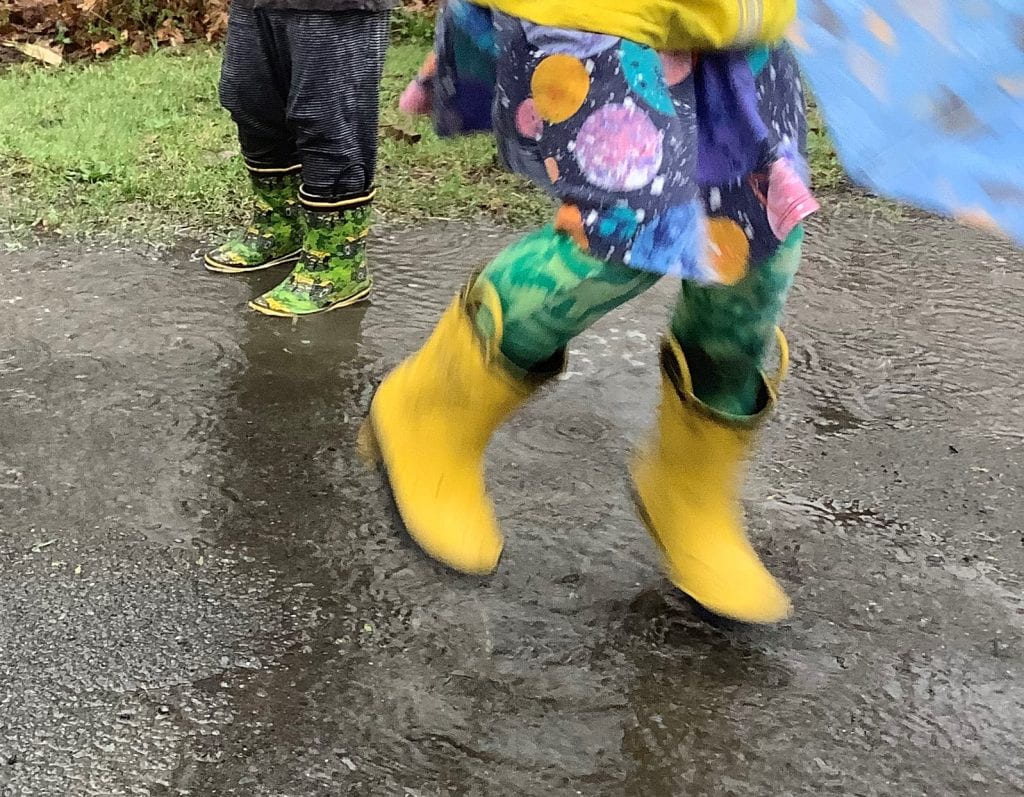 A small child in yellow rain boots jumping in a puddle