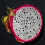 Photo: Cross section of a dragon fruit. It is circular with a thick red skin and a white inner area speckled with lots of little black dots (seeds).