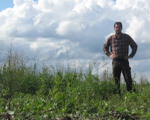 Bryan Brown, Ph.D. stands in an unplanted cornfield where weeds have gone unmanaged
