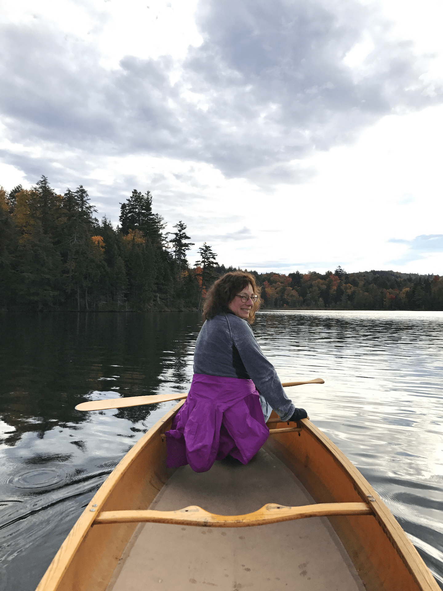 photo of Karen English in the front of a canoe on a lake in the Adirondack Mountains.