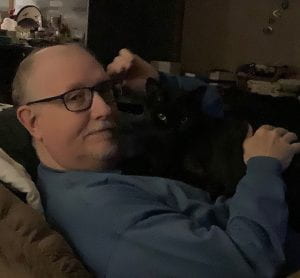 Steve Harris, '76 alumnus sitting on a couch with his cat