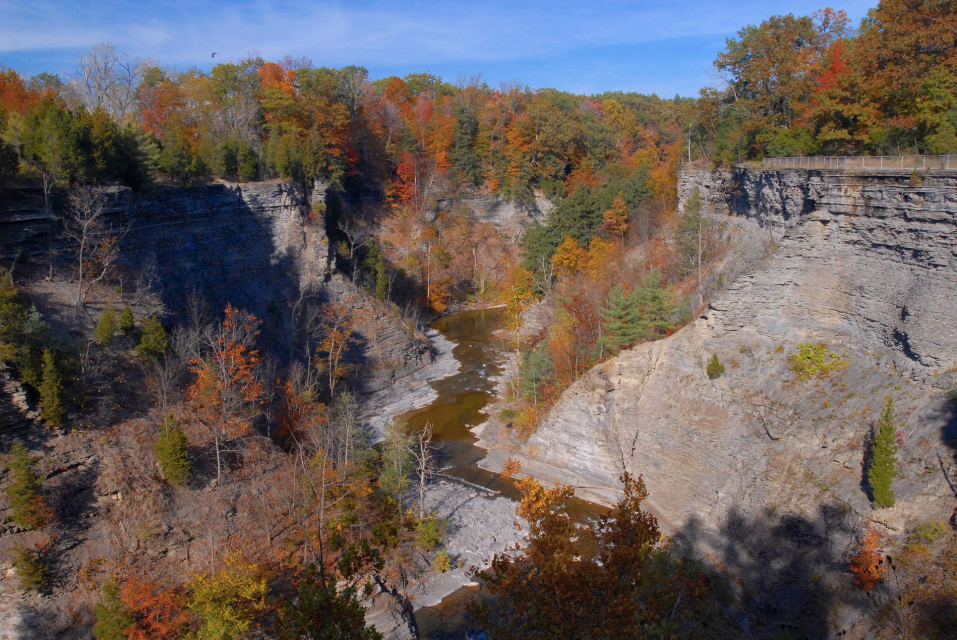 Photo of a hiking trail at Taughannock Falls park, with a winding gorge river and multicolored fall trees